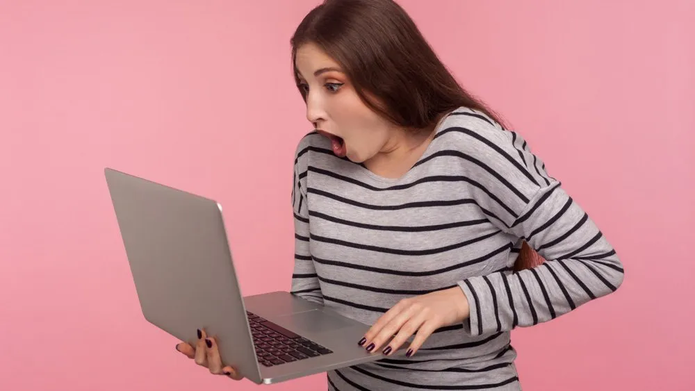 a woman holding a laptop in her right hand.