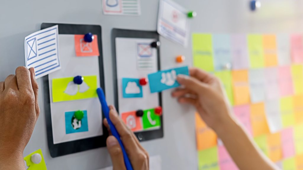 Individuals adding sticky notes to a vertical surface. Elements to include in an effective website design