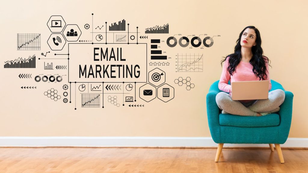 A woman sitting in a chair with a laptop, email marketing written on the wall.