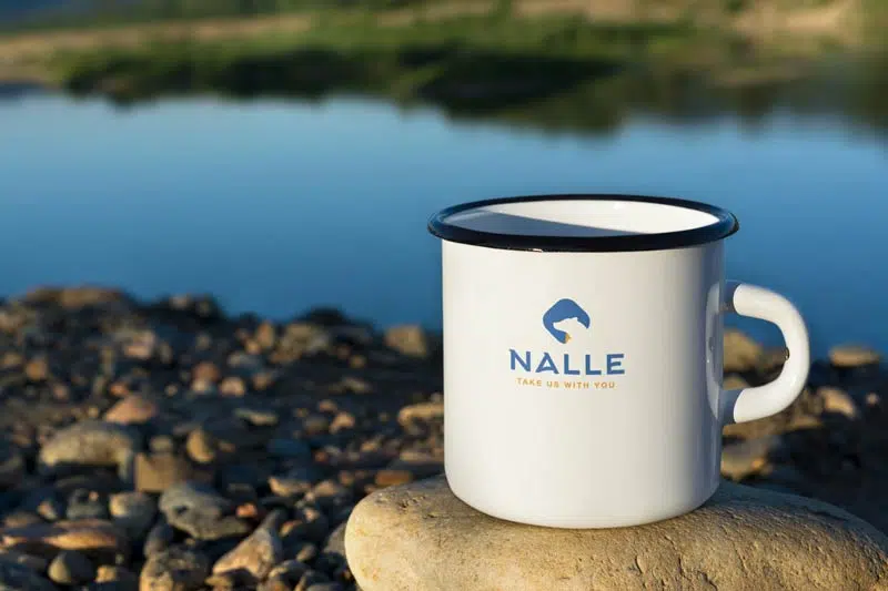 A coffee mug services on a rock next to a lake.