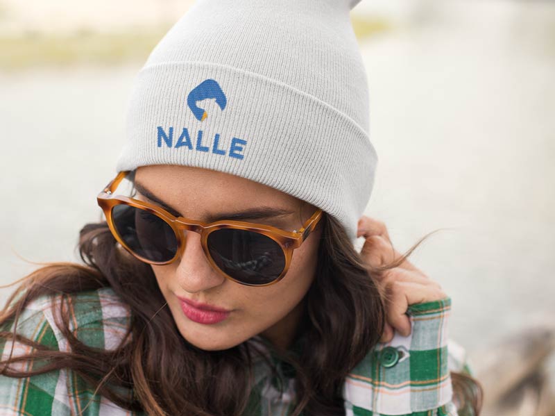 A woman wearing sunglasses and a beanie with the word nale on it poses for a photo.