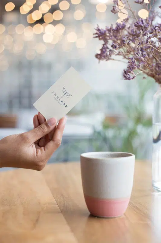 A hand holding a business card next to a cup of coffee at a web design company.