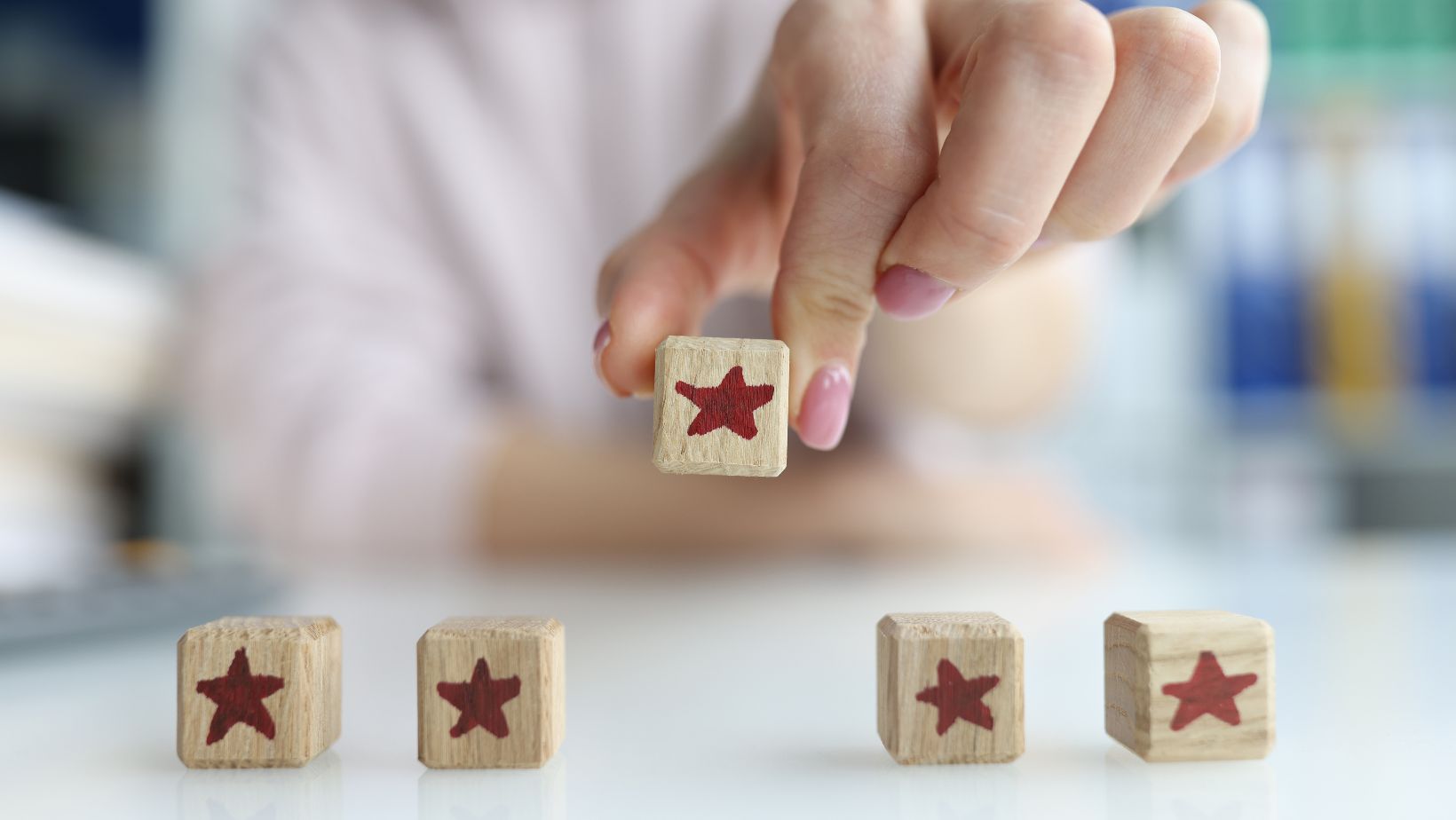 A hand with pink fingernails places a wooden block with a red star among four similar blocks on a white surface, as if sorting through good and bad reviews.