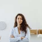 Website VIP Day Professional woman in a white blazer standing confidently in an office with arms crossed.
